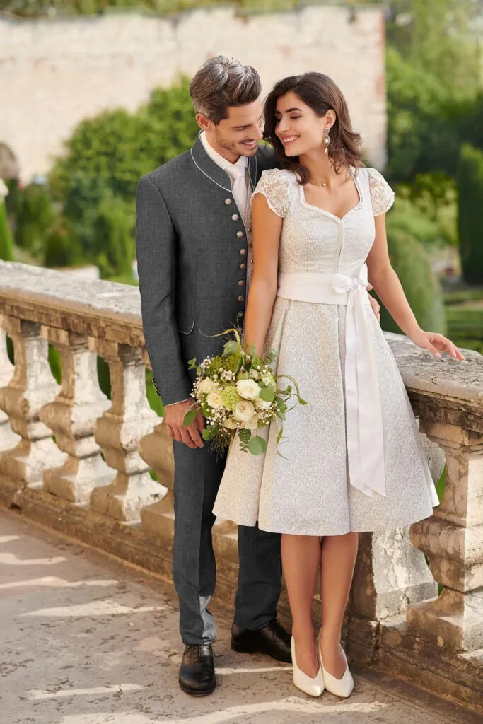 Trachtenhochzeit Pärchen, links Bräutigam im Trachten-Leinenanzug und rechts Braut im Trachten Hochzeitskleid ohne Bluse