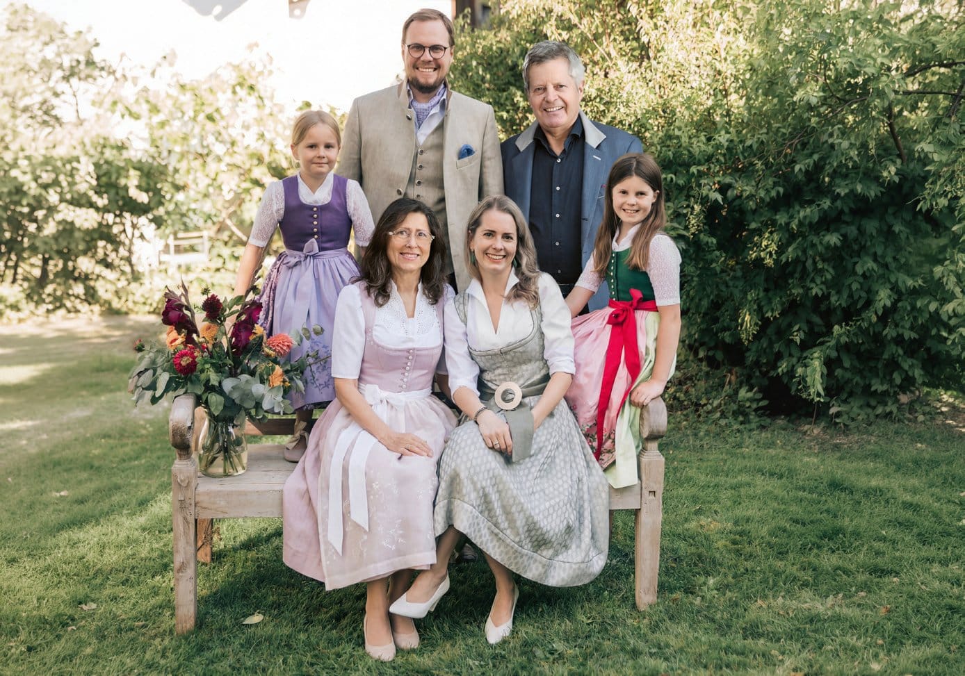 Familie Wimmer im festlichen Trachtenlook auf einer Gartenbank – Designmanufaktur aus Salzburg seit 1741
