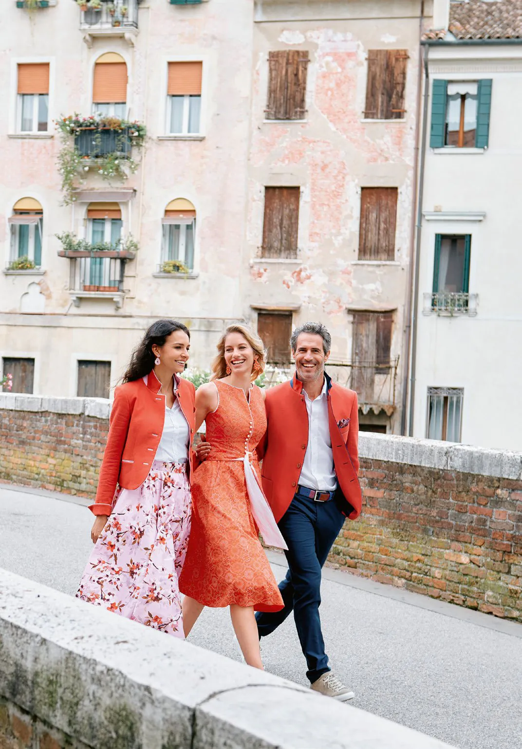 Drei Personen in Apricot-Tracht beim Spaziergang vor italienischer Kulisse – Kollektion Wimmer schneidert