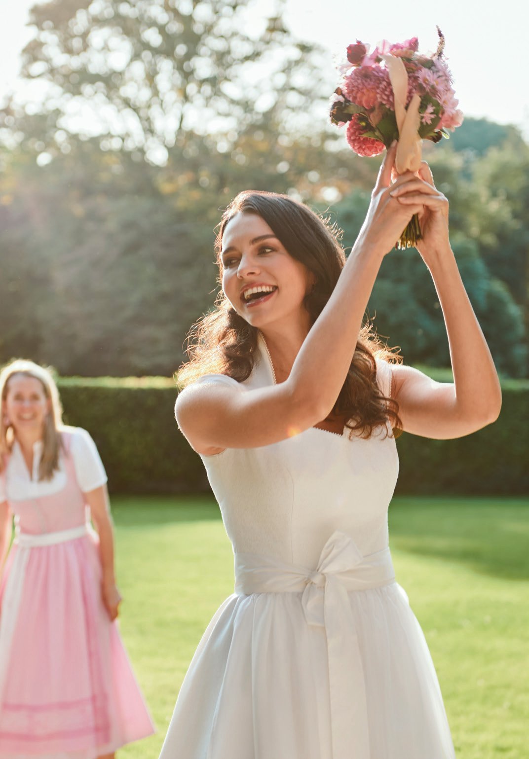 Braut wirft Blumenstrauß in die Höhe auf grünem Gartenrasen in weißem Hochzeitskleid – Wimmer schneidert Hochzeit