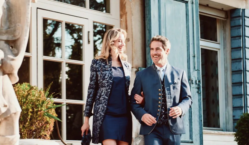 Elegantes Paar in Trachtenmode auf der Treppe einer Villa mit rotem Teppich