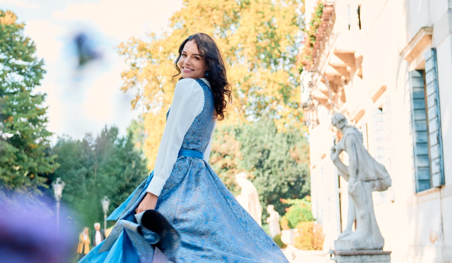 Frau in blauem Dirndl dreht sich lachend auf dem Hof einer italienischen Villa