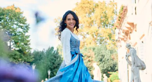 Strahlende Frau in blauem Dirndl dreht sich vor Villa mit Skulptur in Treviso