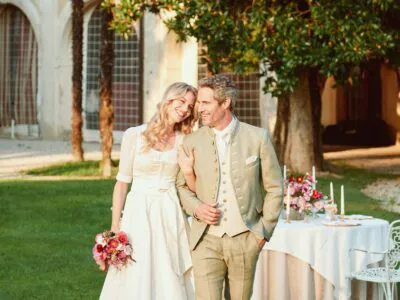 Elegantes Paar vor blühendem Bogen im Garten, klassische Mode in idyllischer Umgebung